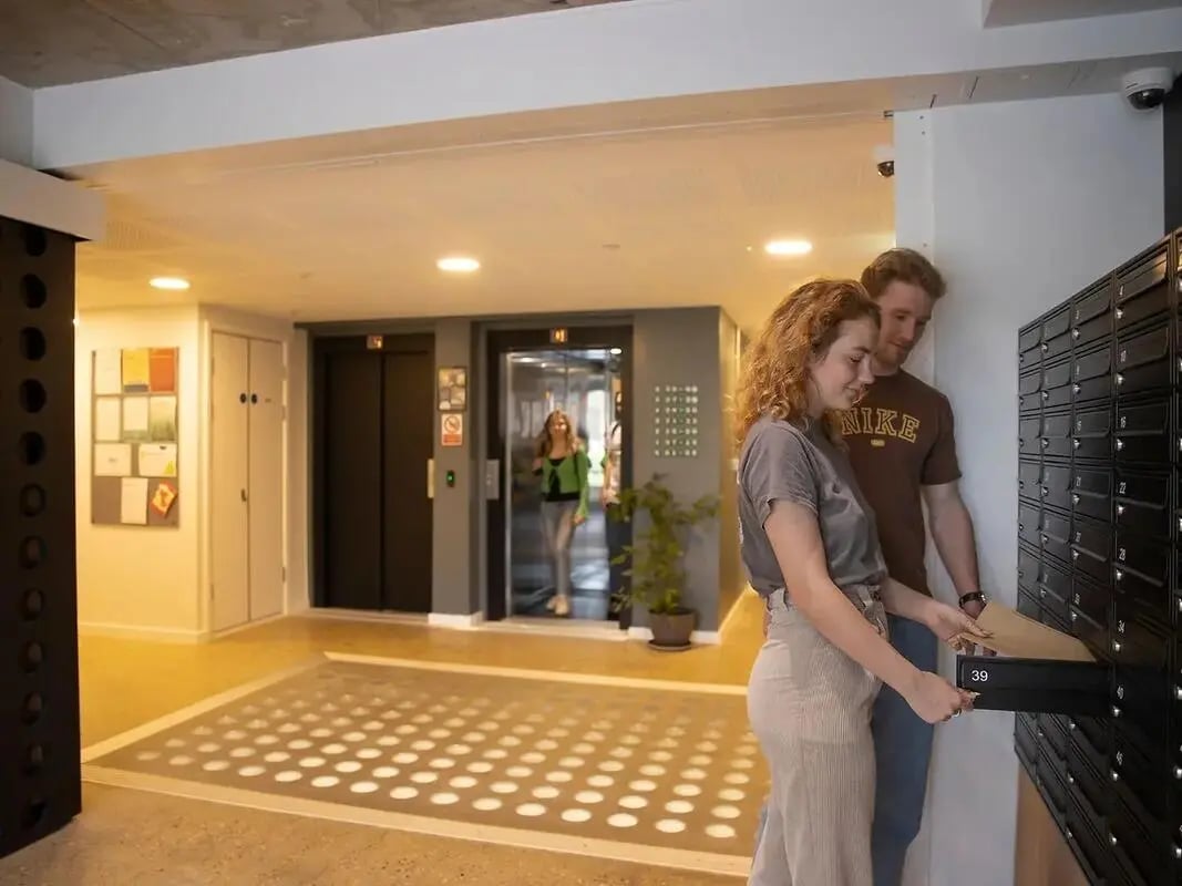 Young couple at mailboxes in apartment building interior at Element Bermondsey in London Student Accommodation
