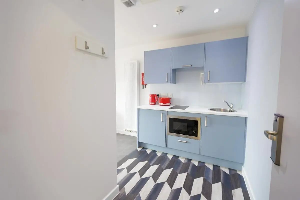 Blue cabinets microwave sink stovetop kitchen at AXO New Cross in London Student Accommodation