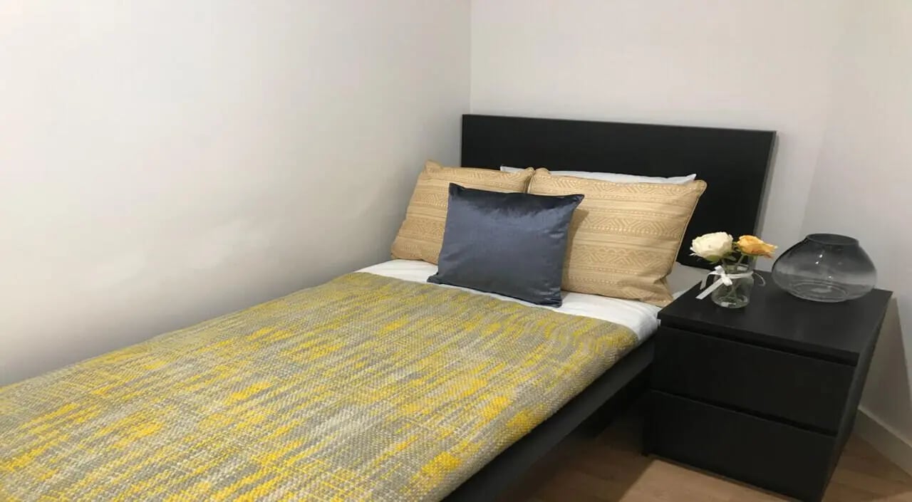 Bed with yellow blanket dark pillows bedside table bedroom at Keele House in Newcastle Under Lyme Student Accommodation