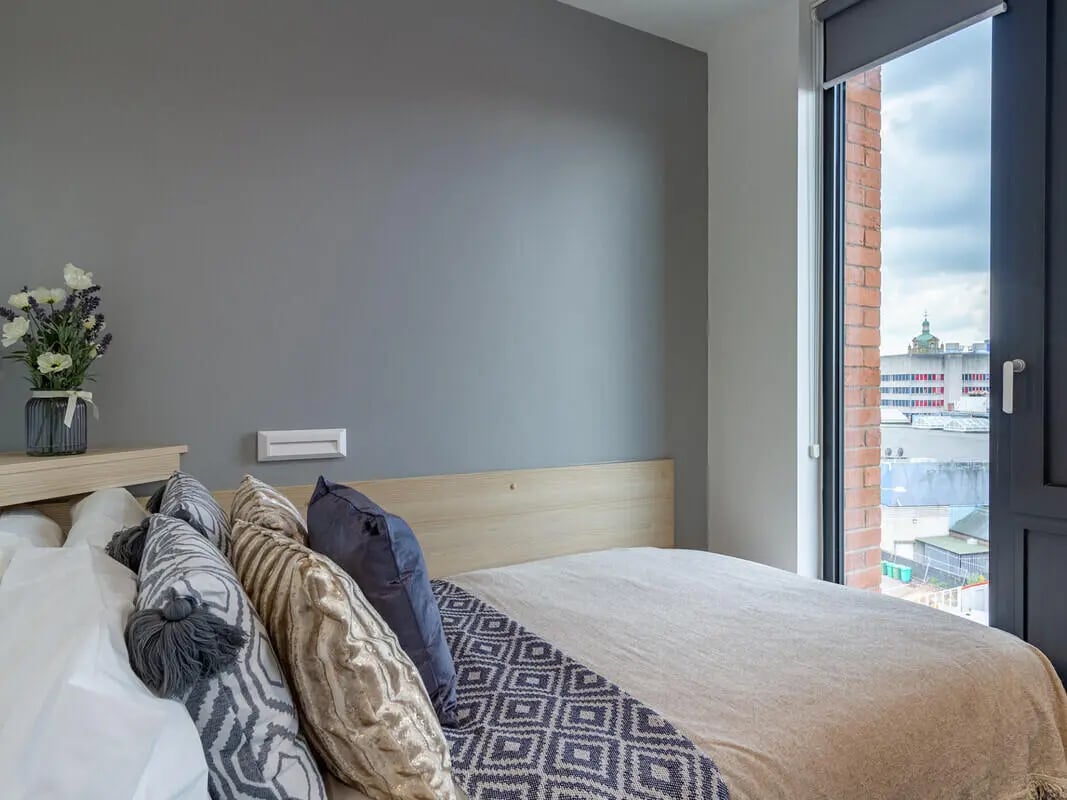 Bed with patterned pillows and cityscape view bedroom at Straits Village in Nottingham Student Accommodation