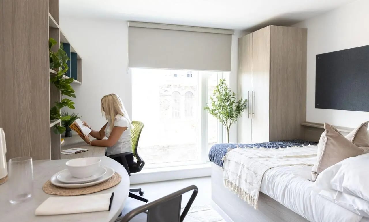 Woman studying at desk beside bed bedroom at Timber Yard in Bristol Student Accommodation