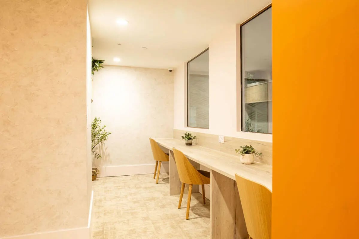Wooden chairs at long desk with plants Study area at Yugo Crown Place in Birmingham Student Accommodation