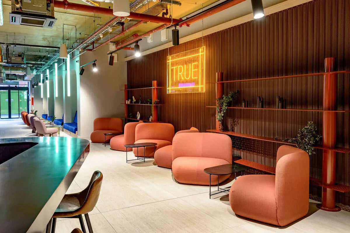 Orange sofas neon sign shelving communal lounge at True Nottingham in Nottingham Student Accommodation