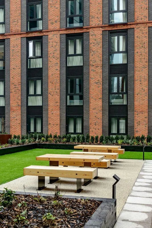 Wooden picnic tables on gravel patio exterior at True Nottingham in Nottingham Student Accommodation