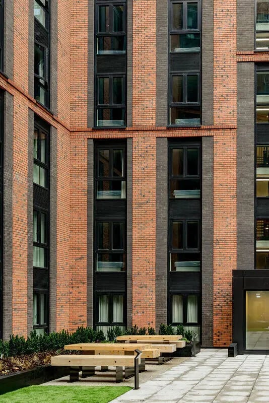 Wooden picnic tables outside modern brick building exterior at True Nottingham in Nottingham Student Accommodation