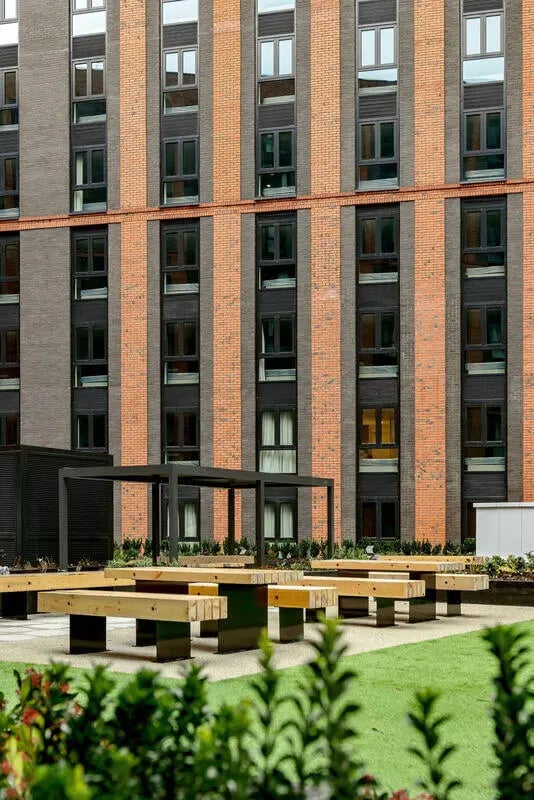 Wooden picnic tables with modern building exterior. at True Nottingham in Nottingham Student Accommodation