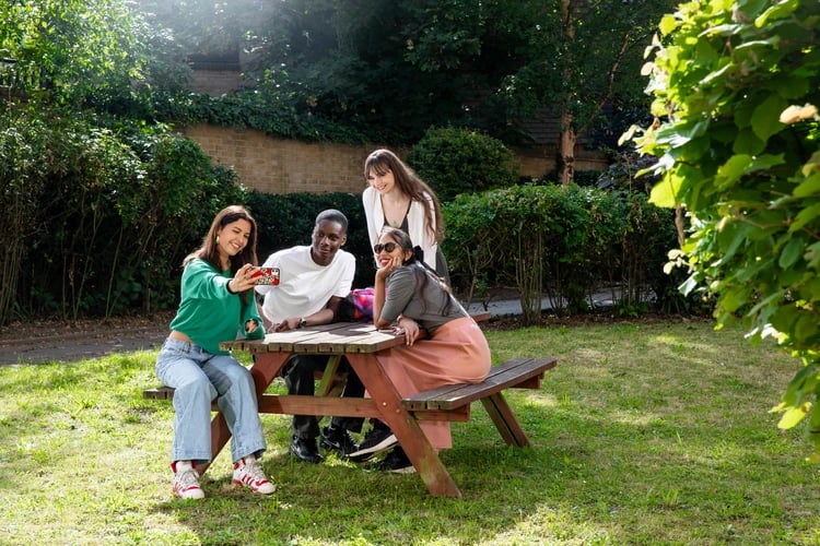 Four students taking a selfie at picnic table exterior at Ewen Henderson Court in London Student Accommodation