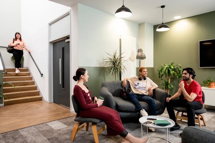 Students socializing on sofa near stairs living room at Blithehale Court in London Student Accommodation