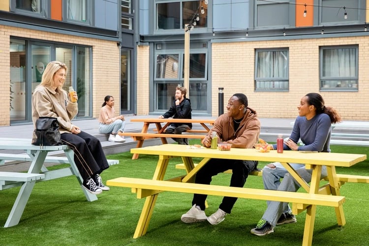 Students eating at picnic tables on lawn exterior at Blithehale Court in London Student Accommodation