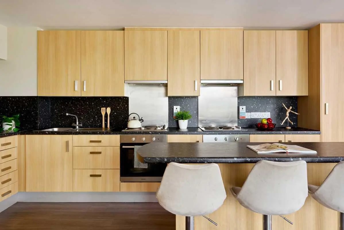 Kitchen with light wood cabinets stovetop sink and stools Kitchen at Millennium View in Coventry Student Accommodation