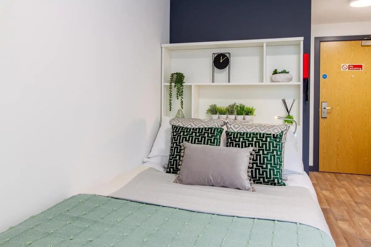 Bed pillows shelf clock and plants bedroom at Plymouth Cross House in Plymouth Student Accommodation