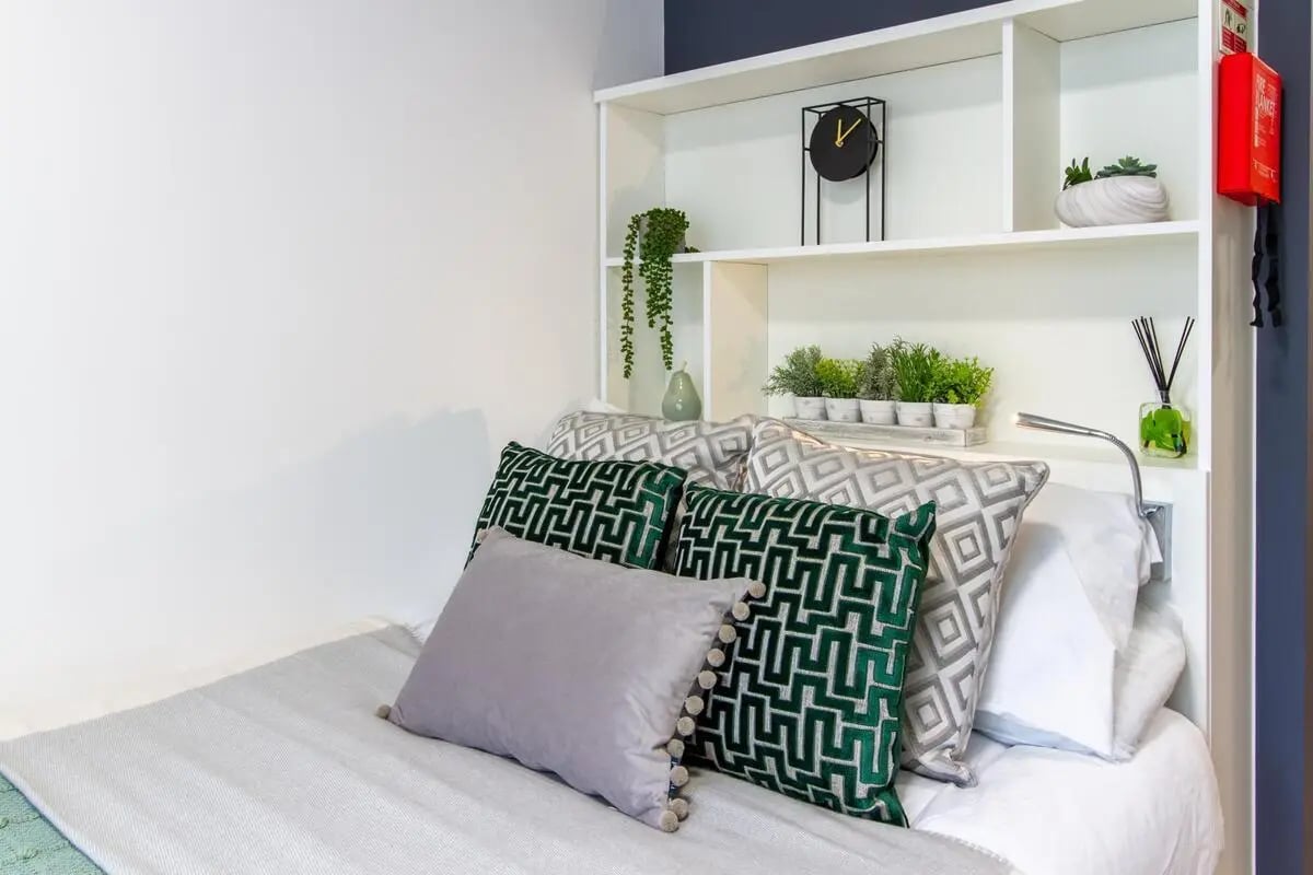 Bed with green patterned pillows and shelves bedroom at Plymouth Cross House in Plymouth Student Accommodation