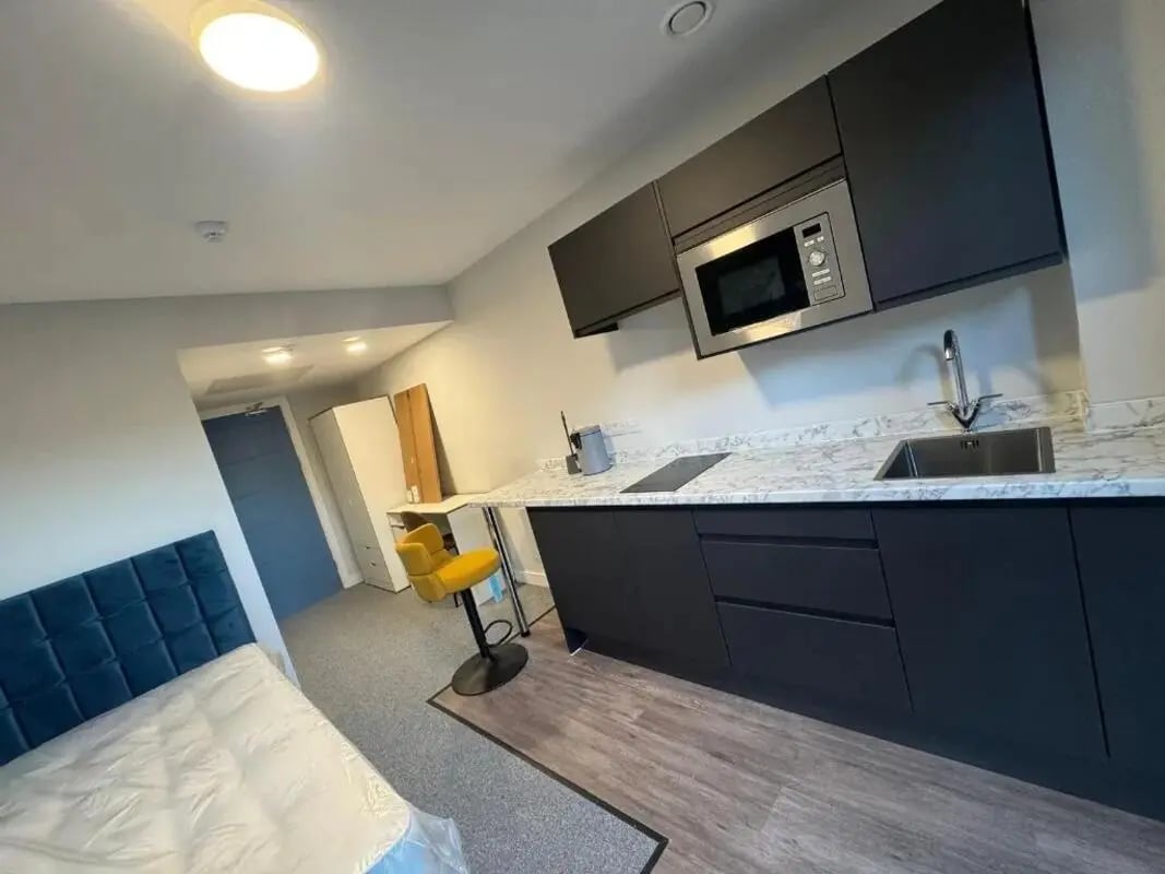 Bed blue headboard kitchen counter sink microwave yellow stool kitchen at Cleveland Apartments in Wolverhampton Student Accommodation