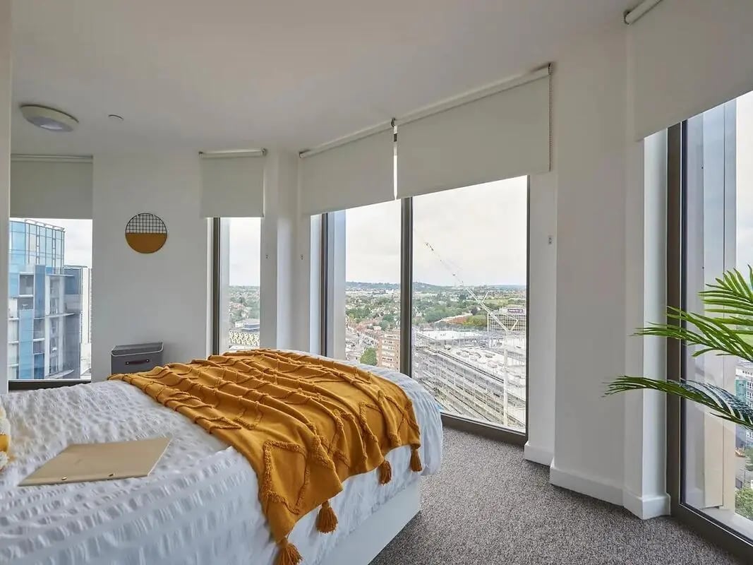 Bed with yellow throw large windows cityscape bedroom at Felda House in Wembley Student Accommodation
