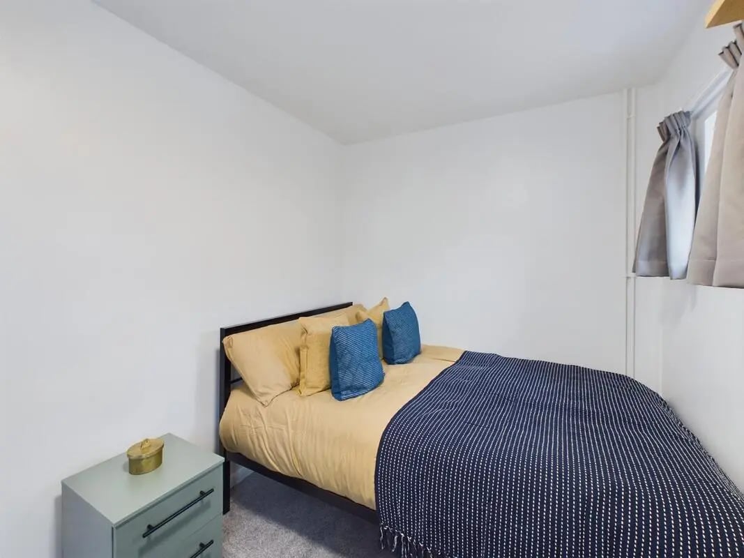 Bed with yellow and blue pillows bedside table bedroom at 6 Bedroom House at 1, Sage Road in Leicester Student Accommodation
