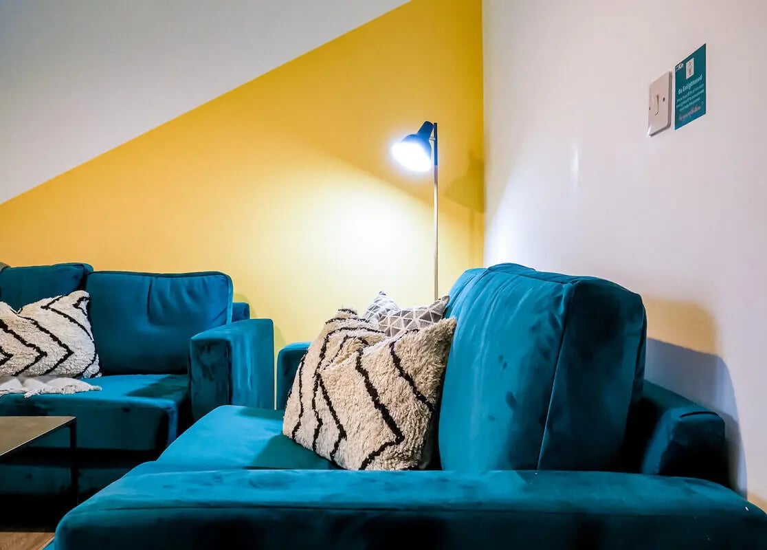 Teal sofas with patterned pillows floor lamp living room at 5 Bedroom House at 14, Driffield Street in Manchester Student Accommodation