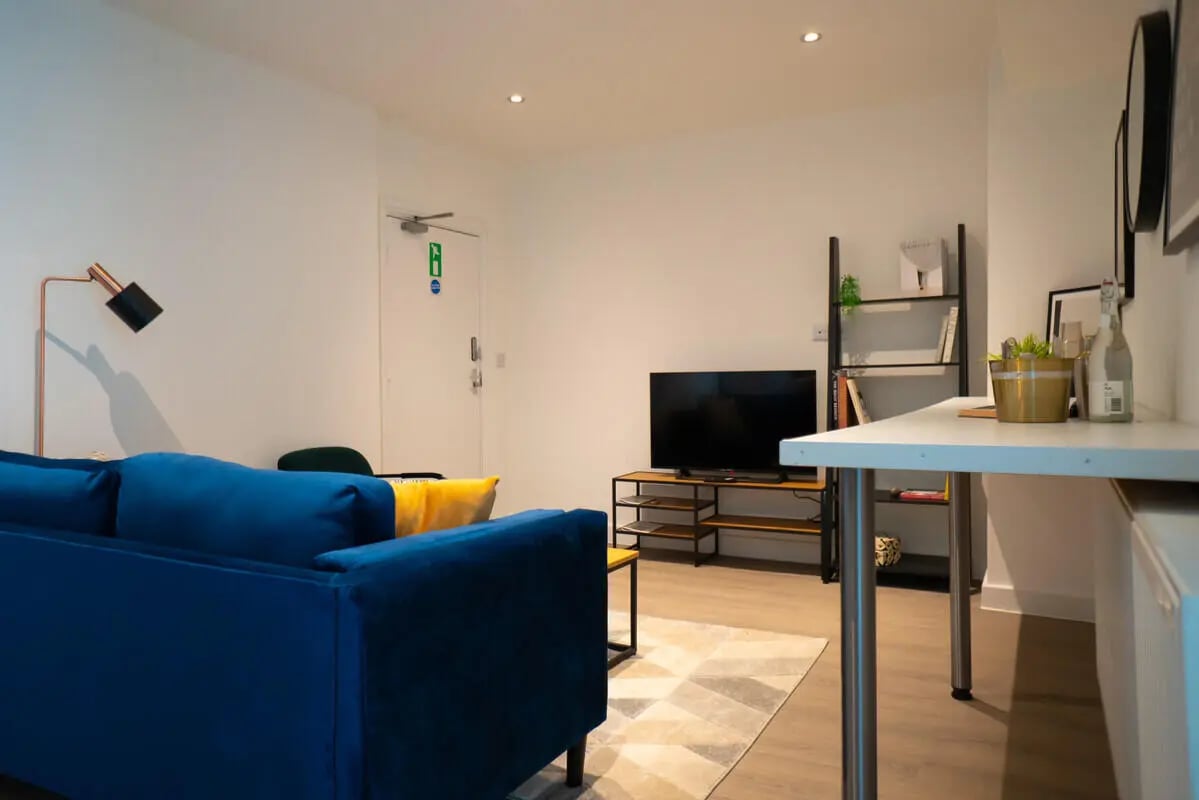 Blue sofa lamp TV shelf and desk living room at 5 Bedroom House at 6, Maine Road in Manchester Student Accommodation