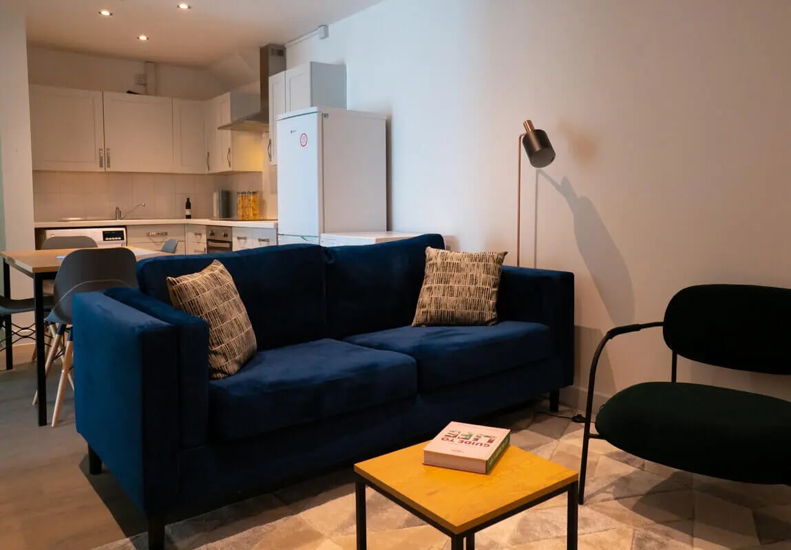 Blue sofa kitchen area chair and table living room at 8 Bedroom House at 71, Monks Road in Lincoln Student Accommodation