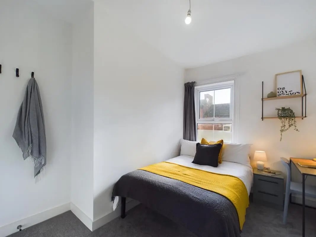 Bed with yellow throw dark pillows desk bedroom at 6 Bedroom House at 32, Monks Road in Lincoln Student Accommodation