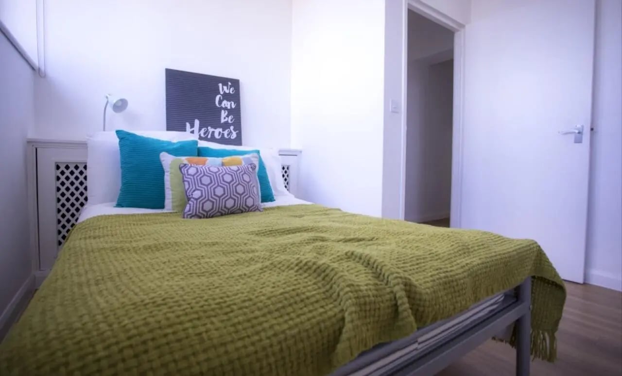 Bed with green throw pillows and sign bedroom at Portobello Garrow House in London Student Accommodation