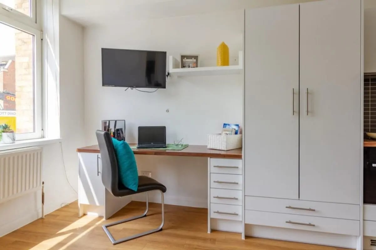 Desk chair laptop television white wardrobe living room at Portobello Garrow House in London Student Accommodation