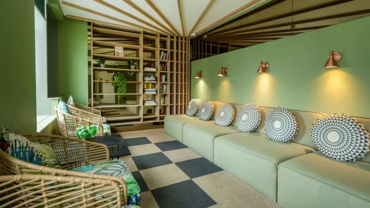 Rattan chairs light green sofa patterned cushions living room at Flora Building - Hoxton in London Student Accommodation