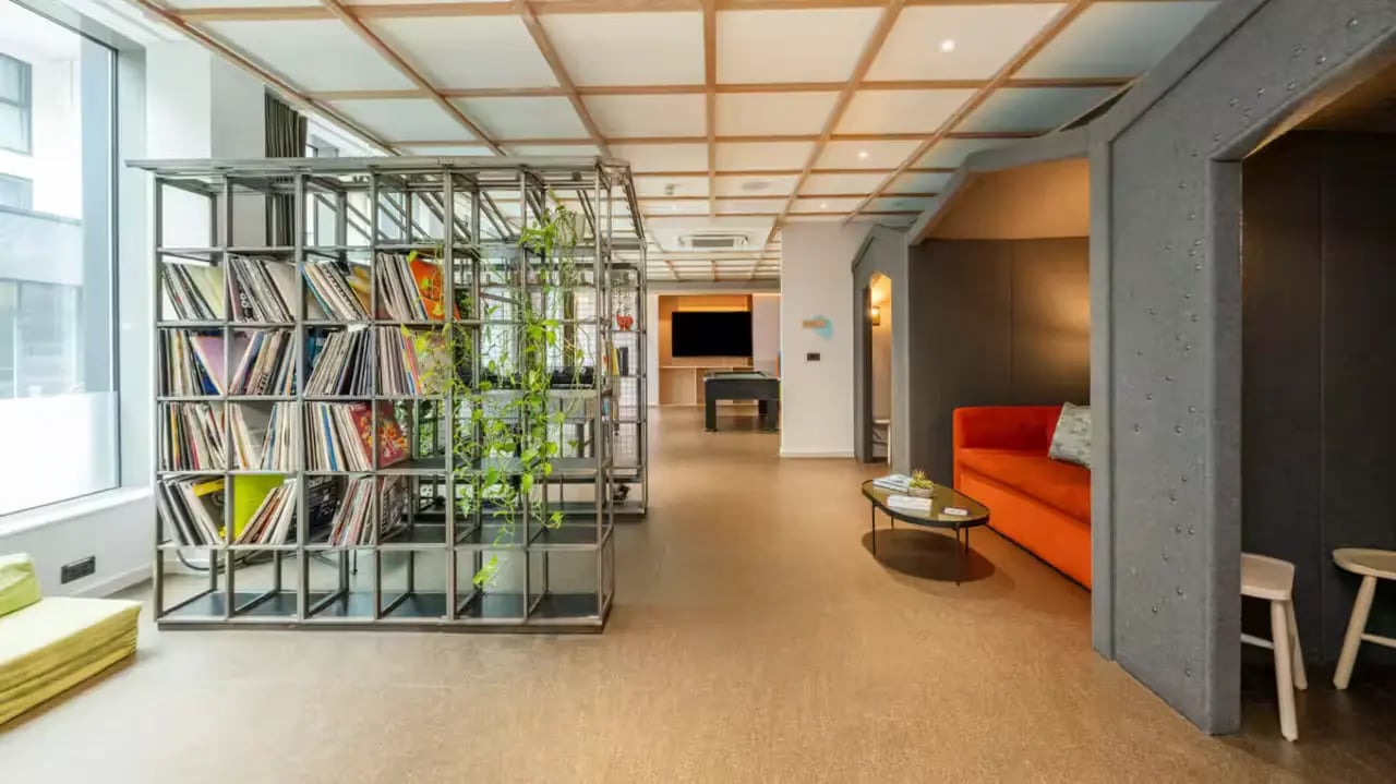 Metal bookshelf with plants and orange sofa living room at Flora Building - Hoxton in London Student Accommodation