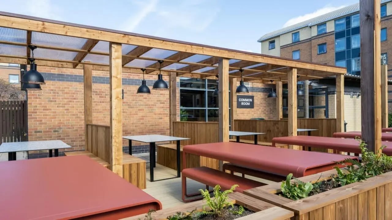 Outdoor seating area with tables and benches common room exterior at Clarence Dock Village in Leeds Student Accommodation