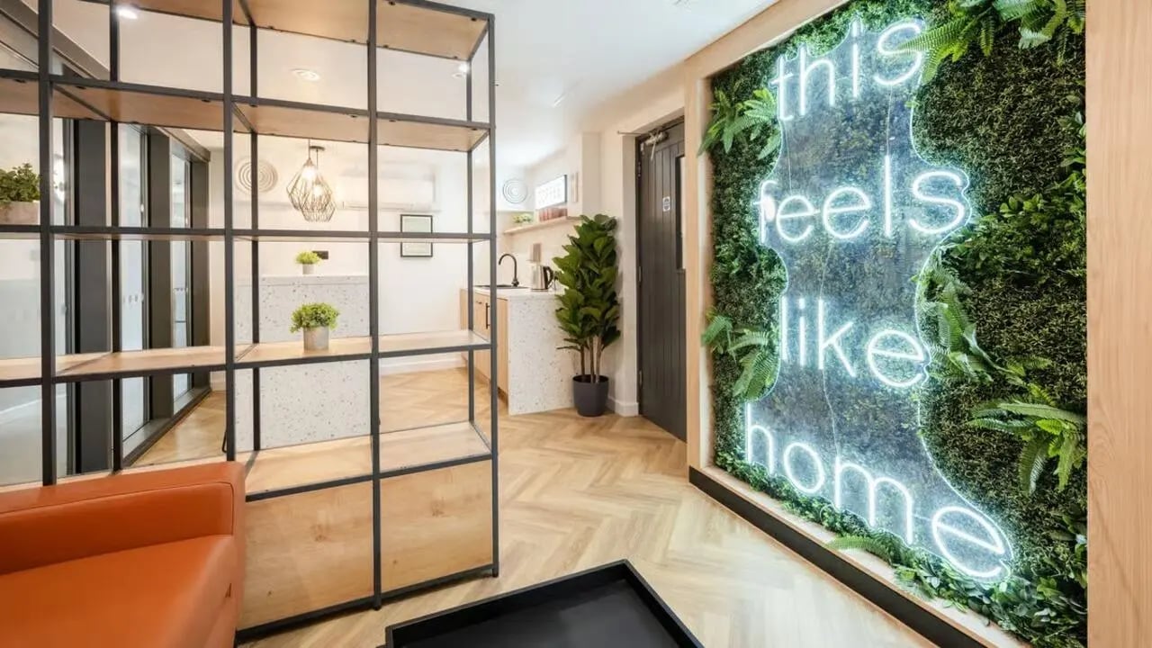 Shelving unit neon sign and plant wall lounge area at Curzon House in Nottingham Student Accommodation