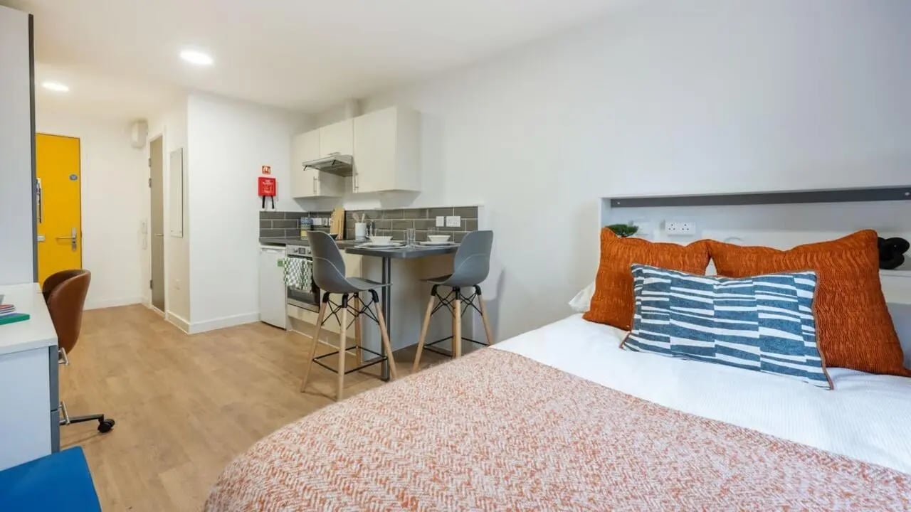 Bed kitchen desk orange pillows studio apartment at Foundry Courtyard in Glasgow Student Accommodation