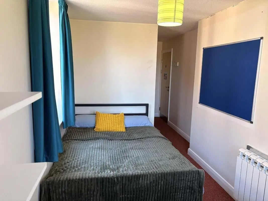 Bed with blue curtains and bulletin board bedroom at Pin Hill in Canterbury Student Accommodation