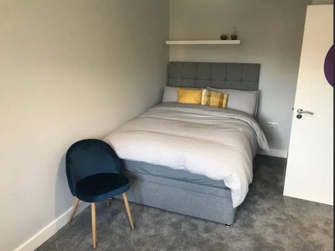 Bed grey headboard yellow cushions blue chair bedroom at Varsity Beeston in Nottingham Student Accommodation