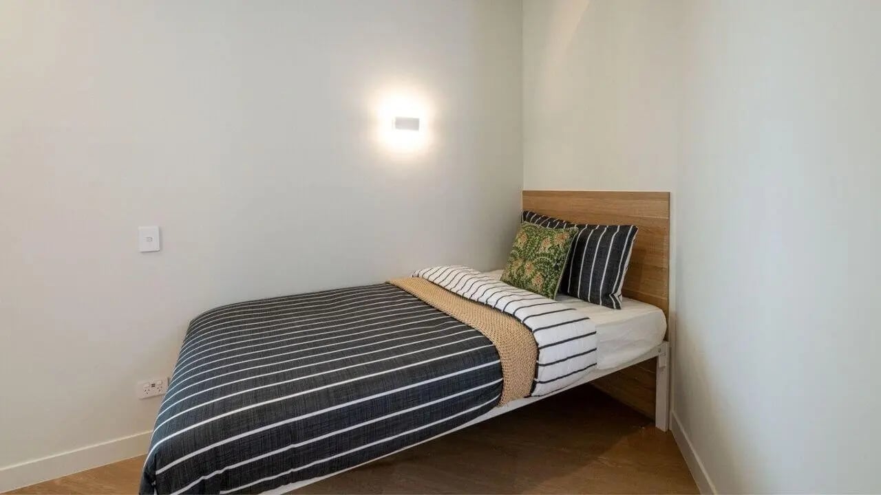 Bed with striped duvet wooden headboard and pillows Bedroom at UniLodge Brisbane City in Brisbane Student Accommodation