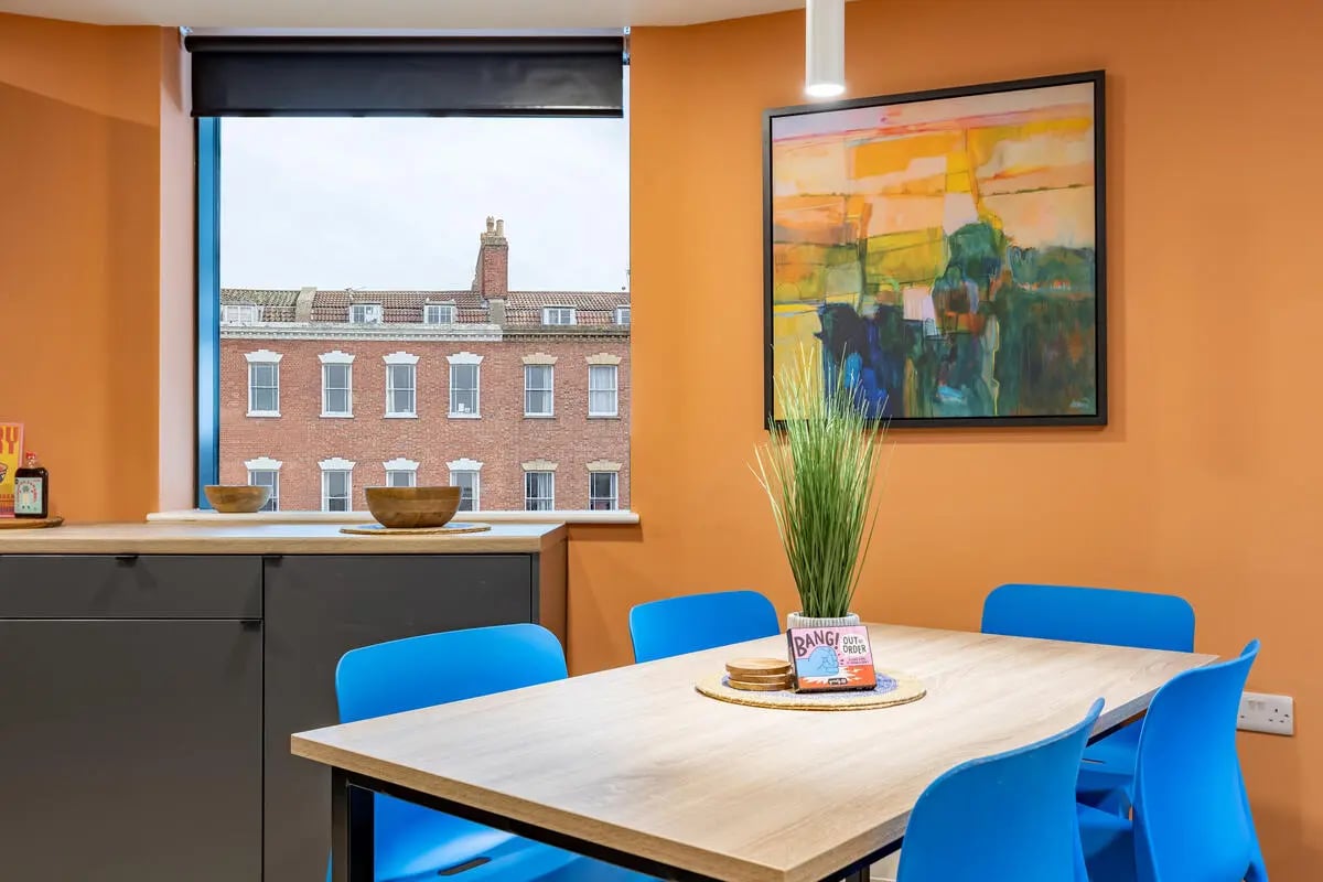 Dining table blue chairs artwork and kitchen area at Croft Court in Bristol Student Accommodation