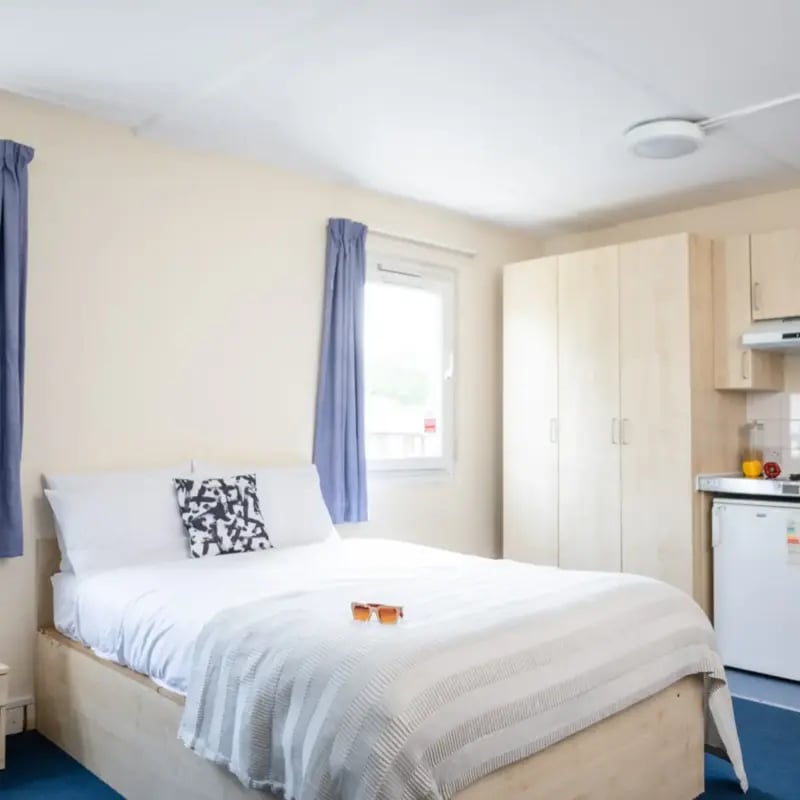 Bed with white linens wardrobe and kitchen area bedroom at Mcmillan student Village in Greenwich Student Accommodation