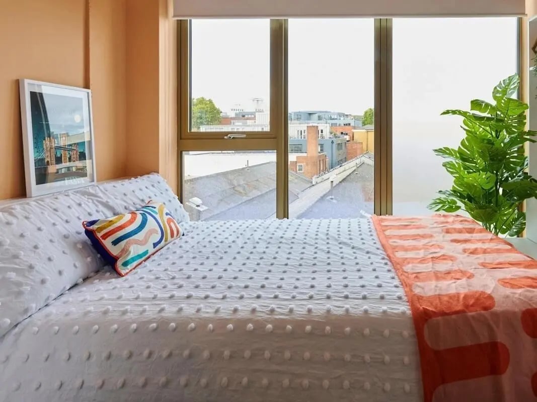 Bed with white duvet colorful pillow plant bedroom at View Studios in London Student Accommodation