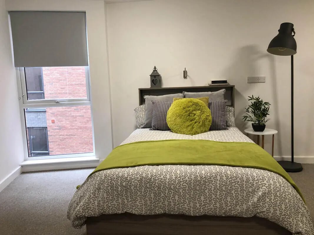 Bed with green throws pillows and window bedroom at Q Studios in Stoke-On-Trent Student Accommodation