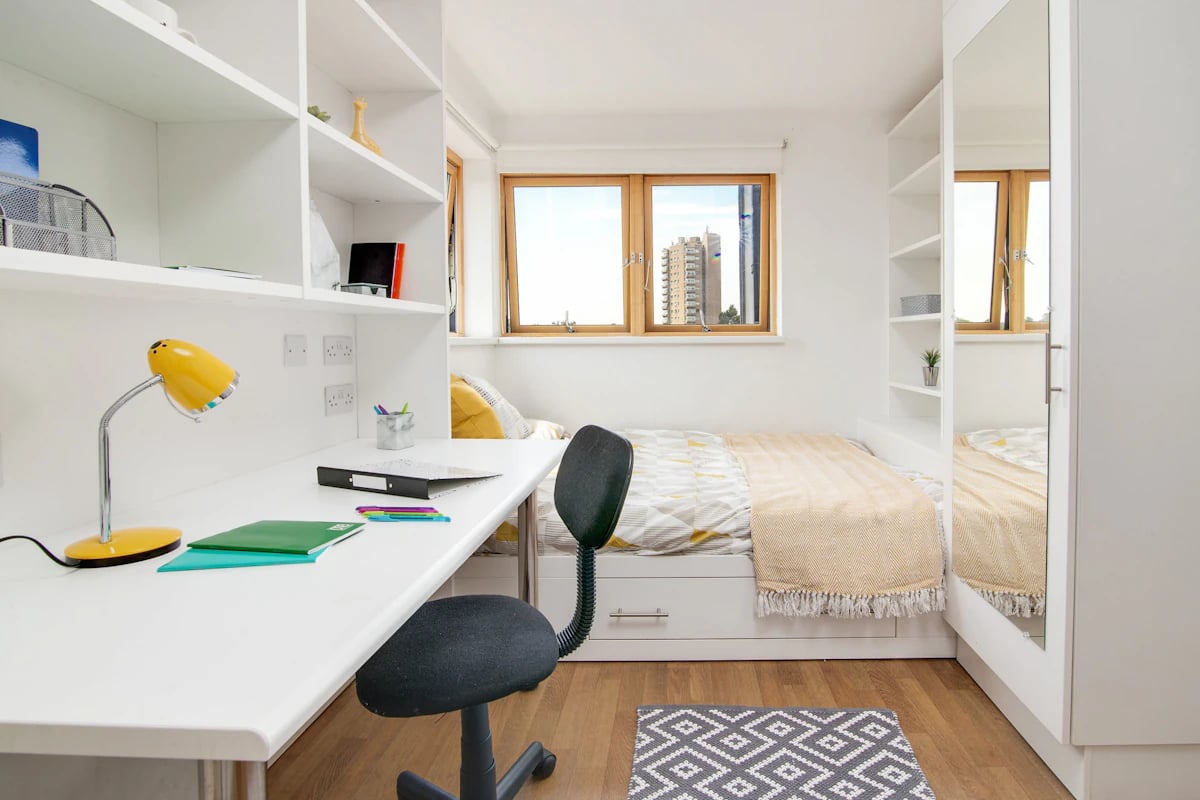 Desk lamp bed shelves with books and desk bedroom interior at Academic House in London Student Accommodation