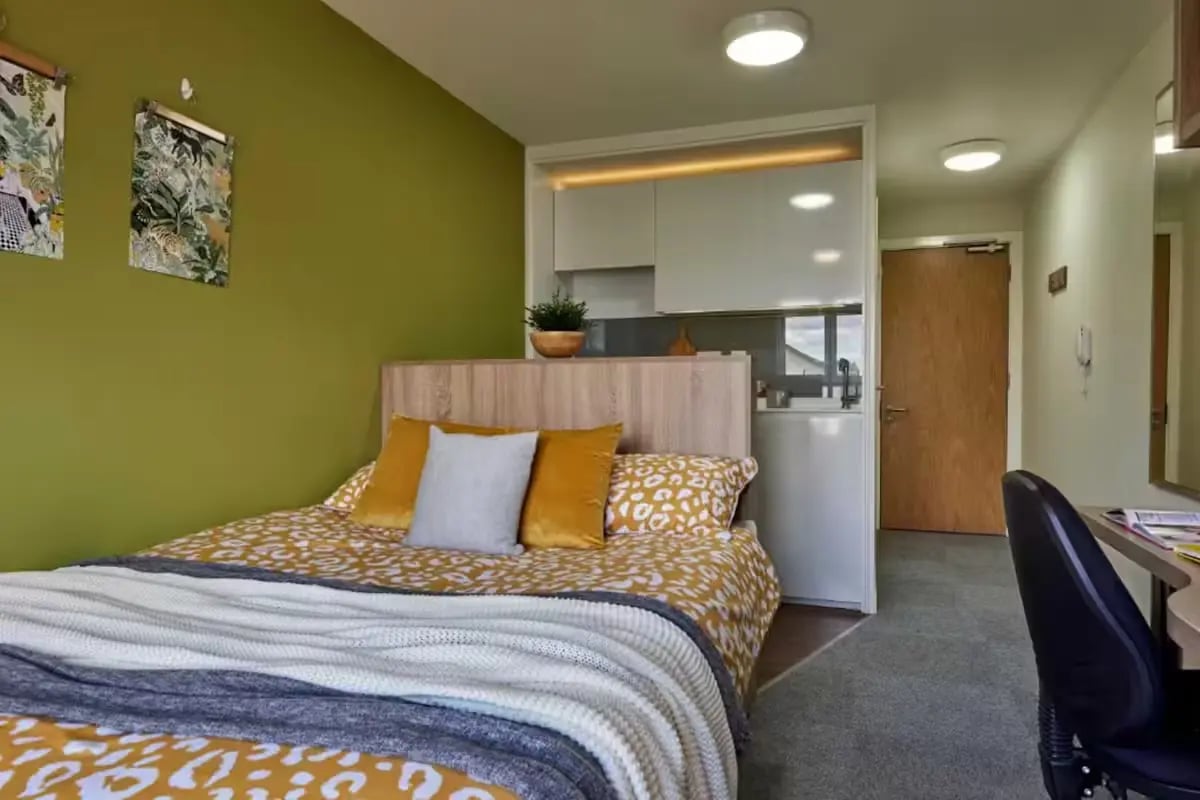 Bed with yellow pillows mini-kitchen and desk bedroom at Selly Oak Court in Birmingham Student Accommodation