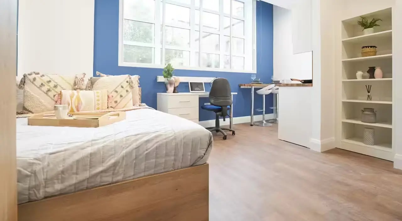 Bed pillows desk chair laptop shelving and stools studio apartment at St Leonard's House in Lancaster Student Accommodation
