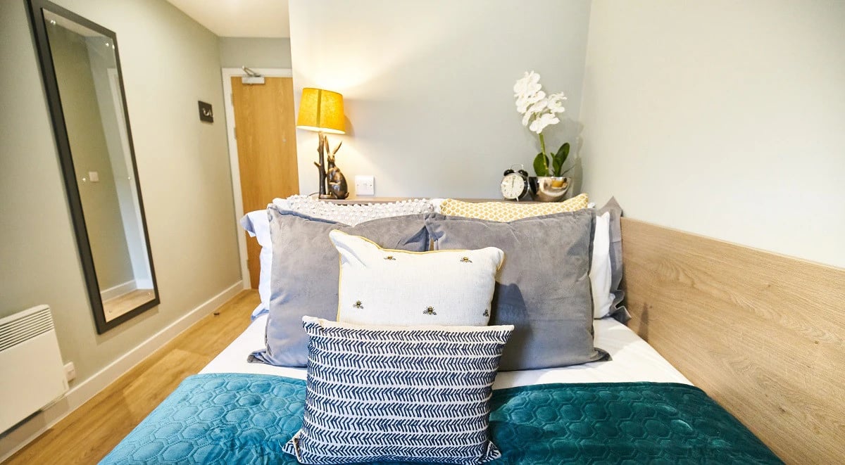 Bed with grey pillows teal throw mirror and lamp bedroom at Symons House in Leeds Student Accommodation
