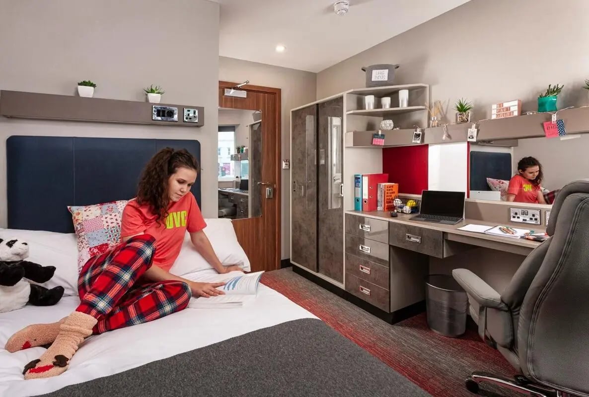 Woman reading on bed with desk and closet bedroom at Study Inn Talbot Street Nottingham in Nottingham Student Accommodation