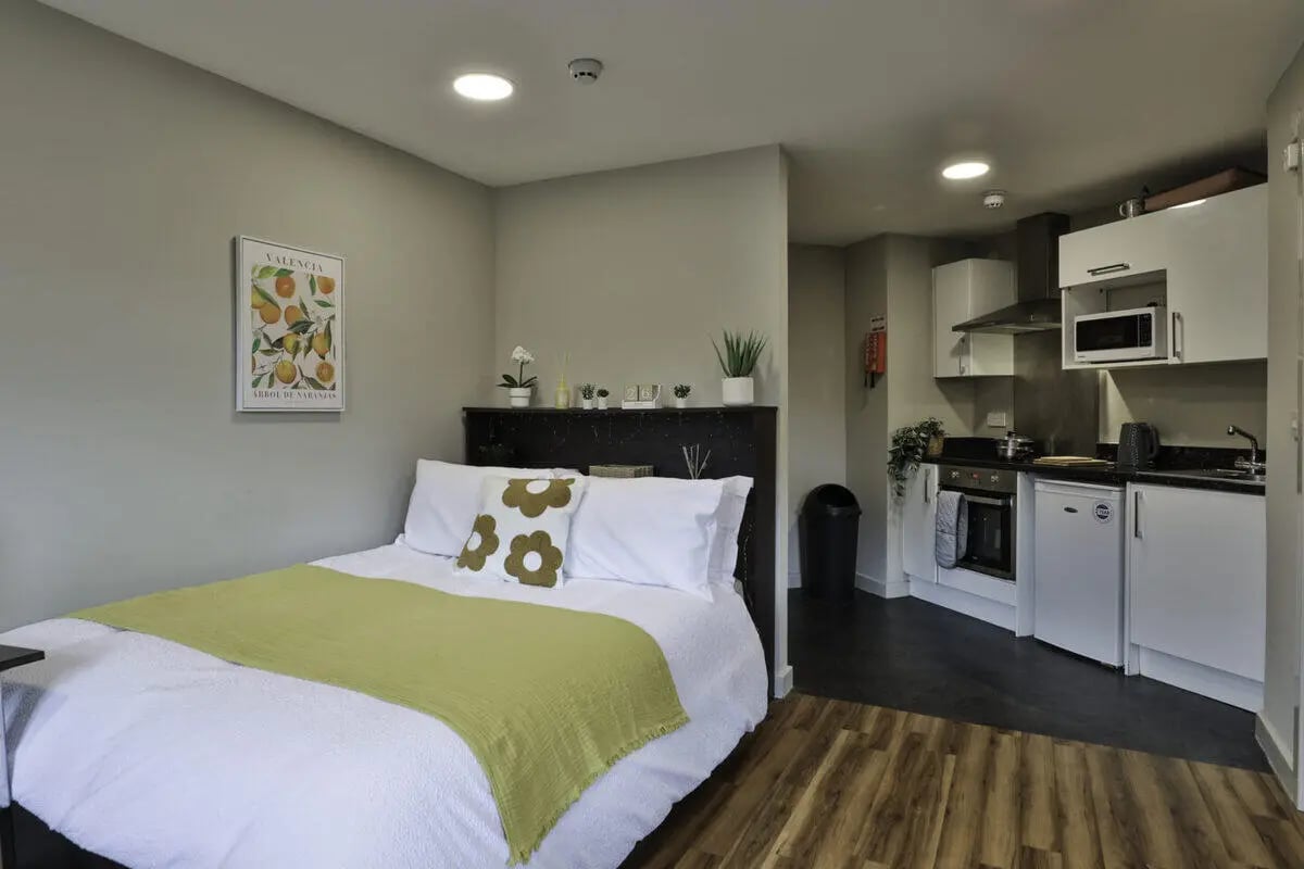 Bed with green throw and kitchen area studio at Ladybarn House in Manchester Student Accommodation