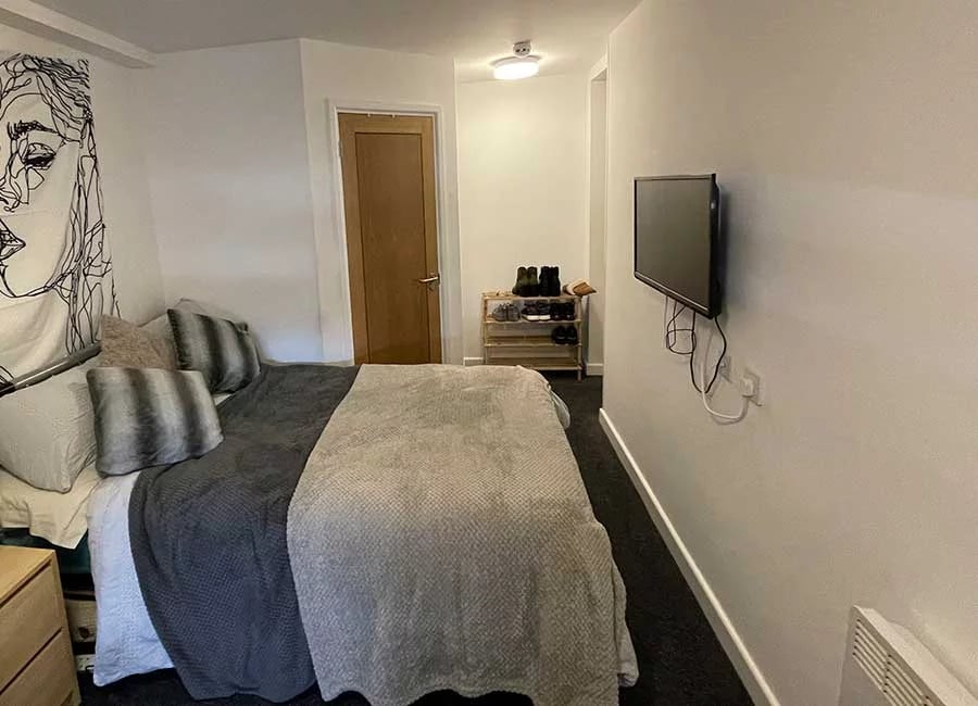 Bed with pillows television shoeshelf and door bedroom at Forest Court in Loughborough Student Accommodation