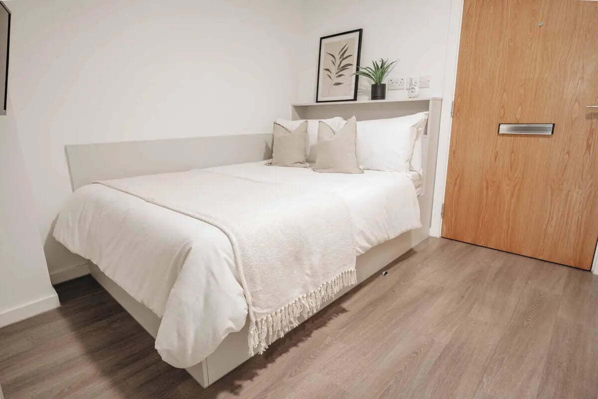Bed with white bedding plant art and door bedroom at Avon Studios in Bath Student Accommodation