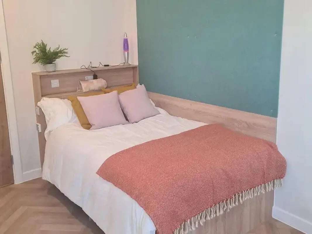 Bed with pink and yellow pillows orange throw Bedroom at Yugo St. Crispin's House in Norwich Student Accommodation