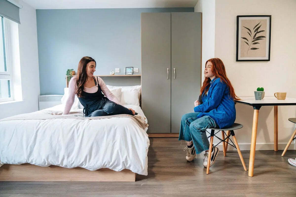 Two women talking in bedroom with bed wardrobe and table at Caledon Court in Aberdeen Student Accommodation