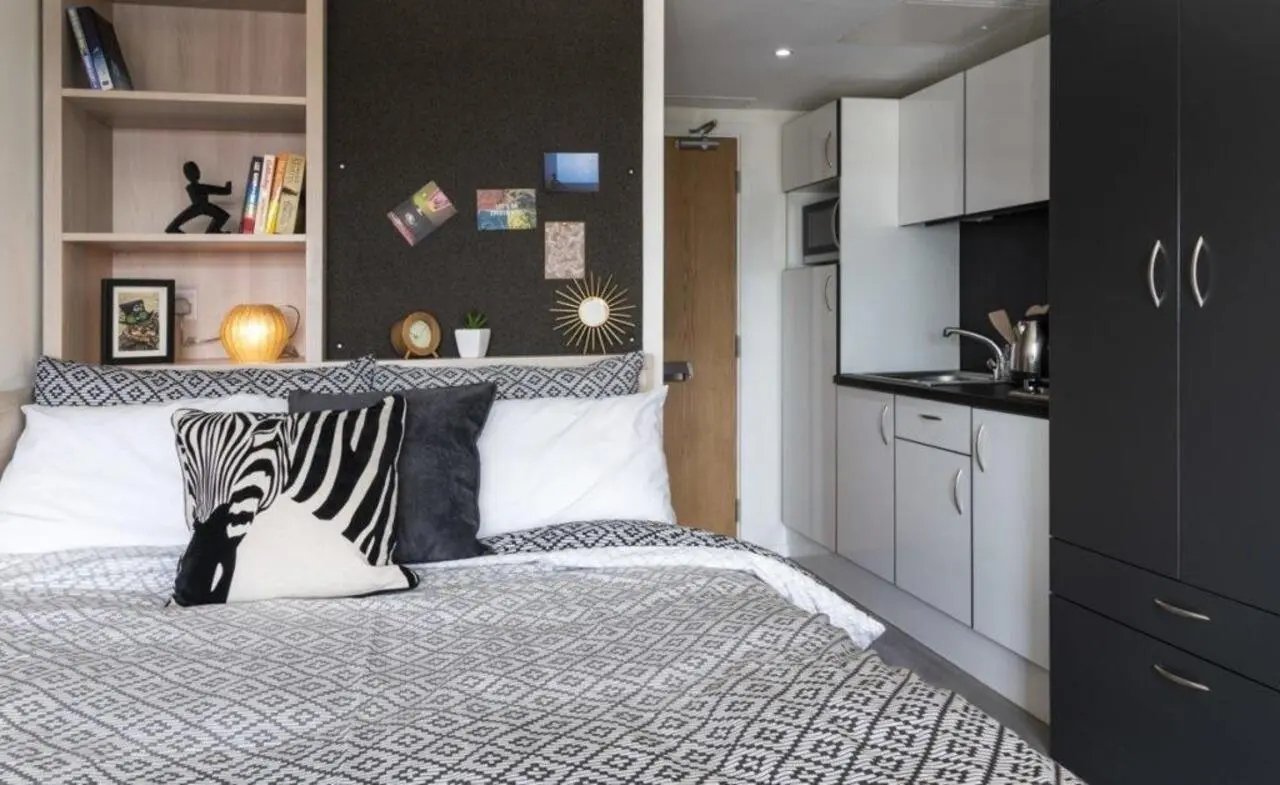 Bed pillows bookcase kitchenette and storage bedroom kitchen at The Lyra in London Student Accommodation