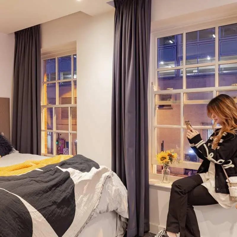 Bed with patterned duvet and woman with phone bedroom at True Birmingham in Birmingham Student Accommodation