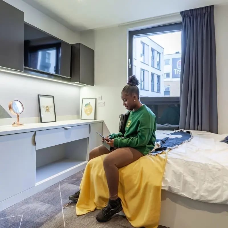 Young woman on bed with desk and TV bedroom at True Birmingham in Birmingham Student Accommodation